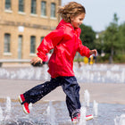 A young child splashes in a water feature wearing Originals Waterproof Trousers Navy and a red raincoat, enjoying an outdoor day.